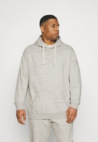 Hoodie gris clair en tissu doux et texturé. Il possède une poche à l'avant, une capuche avec cordon de serrage et des poignets côtelés. Assorti avec un pantalon coordonné.