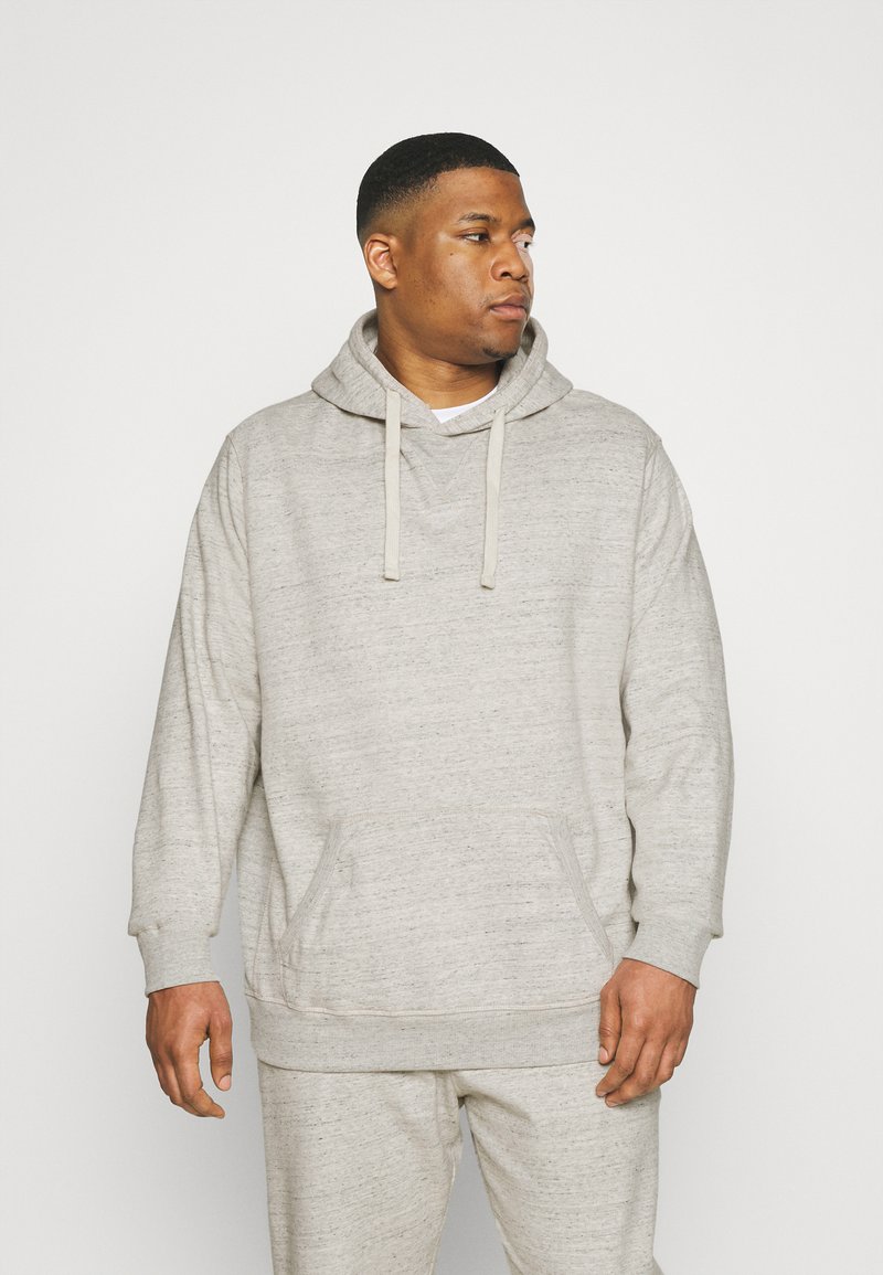 Hoodie gris clair en tissu doux et texturé. Il possède une poche à l'avant, une capuche avec cordon de serrage et des poignets côtelés. Assorti avec un pantalon coordonné.