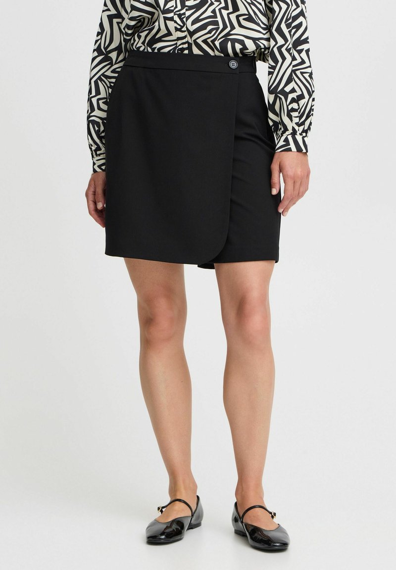 Zwarte wikkelrok met een gladde textuur, voorzien van een sluiting met zijknop. Gecombineerd met een gebloemd blouse en zwarte flats.
