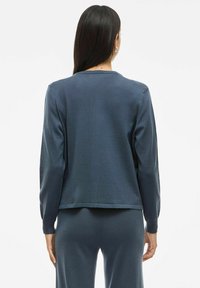 Temno modra, dolgosleeve majica s sproščenim krojem in okroglim ovratnikom; ima mehak material in enostavno šivanje ob robovih in manšetah.