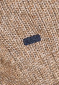 Tissu tricoté beige avec un motif texturé ; une étiquette rectangulaire noire avec "J&Joy" intégrée dans le coin inférieur.