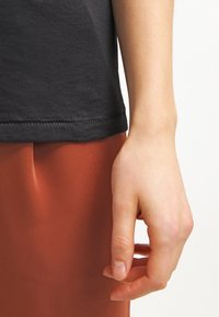 Camiseta de algodón negra con una textura suave, combinada con pantalones de tela color óxido, que muestran un corte relajado y un detalle de costura limpio.