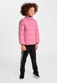 Ljusrosa vadderad jacka med hög krage och horisontell söm; kombinerad med svarta byxor med vita chevronränder.