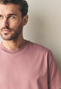 Støvet pink kortærmet T-shirt med rund hals i blødt materiale. Stoffet ser glat ud med minimal tekstur.