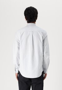 Camisa de manga larga a rayas en algodón azul claro y blanco, con un dobladillo curvado, puños con botón y un pliegue en la parte posterior para mayor libertad de movimiento.