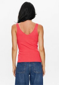 Korallfärgad ribbad linne med V-formad rygg. Har smala axelband och en figurnära silhuett, kombinerad med jeans.