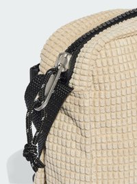 Borsa beige con texture e superficie trapuntata, dotata di una cerniera nera e dettagli della tracolla. Include un moschettone in metallo argentato per fissare gli oggetti.