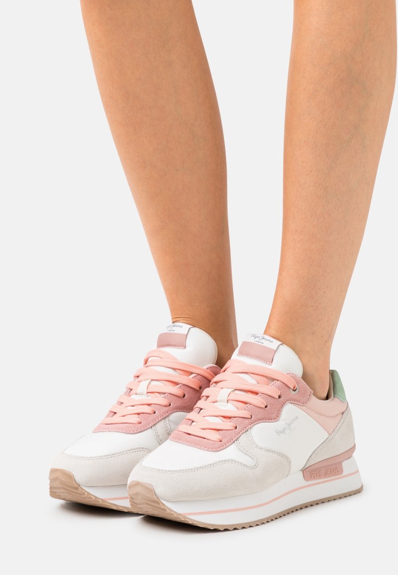 Zapatillas blancas y rosas con materiales de ante y cuero, que presentan una suela texturizada, cordones rosas y un acento en verde menta en el talón.