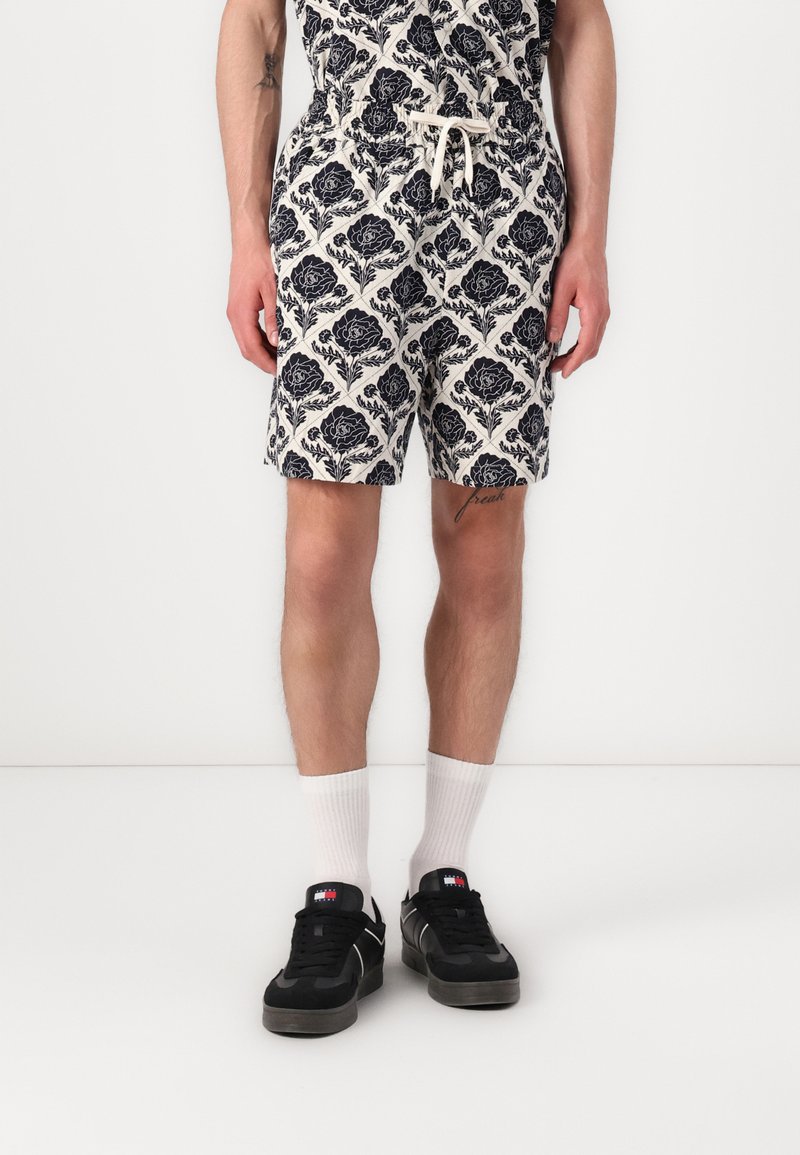 Hvide og marineblå mønstrede shorts med blomsterdesign, elastisk talje og snor. Stylet med hvide sokker og sorte sneakers.
