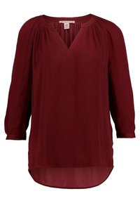 Burgundská blůzka s výstřihem do V, dlouhými rukávy, řasenými detaily na ramenech a zaobleným spodním lemem. Vyrobena z lehkého, splývavého materiálu.