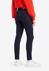 Jeans skinny azul oscuro con una cintura alta, costuras amarillas en contraste y un diseño de bolsillo trasero curvado con etiqueta.