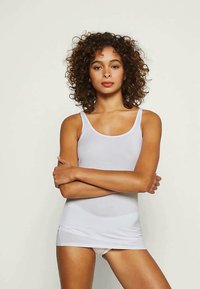 Camiseta blanca sin mangas hecha de tela suave y elástica con escote redondo, diseño ceñido y confección sin costuras, adecuada para superponer.