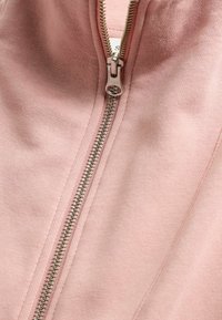 Rosa Kapuzenjacke mit metallischem Reißverschluss, ausgestattet mit einer glatten Textur und einem figurbetonten Design. Der Stoff hat ein weiches, leicht meliertes Aussehen.