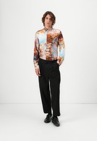 Langärmliges Hemd mit einem abstrakten Muster in Blau-, Braun- und Orangetönen; schwarze Hose; schwarze Schuhe; aus leichtem Stoff.