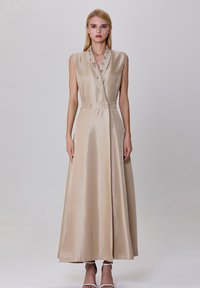 Robe sans manches beige avec un corsage ajusté, ornée de boutons décoratifs et d'une jupe évasée, fabriquée à partir d'un tissu brillant et texturé.