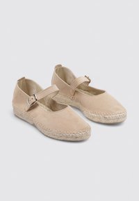 Espadrilles en toile beige avec un bout arrondi, une sangle autour de la cheville et une semelle en jute tissée. Texture lisse avec un design minimaliste.