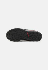 Semelle extérieure en caoutchouc noir avec un motif de traction texturé ; comprend le logo "TRACTION" en rouge. Convient aux activités de plein air.