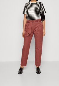 Pantalons rouges taille haute avec ceinture à nouer, associés à un t-shirt rayé noir et blanc, et des chaussures noires à enfiler. Texture de tissu lisse.