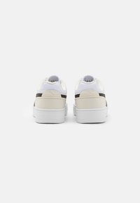 Sneakers bianchi con un design beige e marrone scuro, caratterizzati da una texture in pelle liscia, forma arrotondata e collo imbottito.