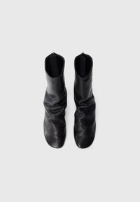 Bottines en cuir noir avec un design ondulé, présentant une texture lisse et un embout arrondi. Fermeture éclair à l'arrière.
