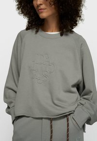 Sweat-shirt gris clair avec logo brodé. Présente un col rond, des épaules tombantes et des poignets côtelés. Tissu doux avec une coupe décontractée.