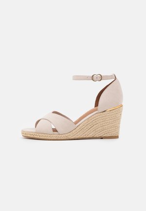 Beige kile-sandal med flettet juteplatform, krydsremme over tæerne, ankelrem med guldbeklædt spænde og moderat hælhøjde.