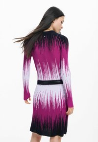 Fazonhoz illeszkedő kötött ruha fekete, rózsaszín és fehér színátmenetes mintával, hosszú ujjakkal és fekete övvel a deréknál.