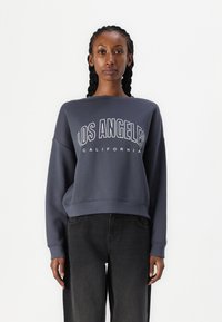 Felpa navy con vestibilità comoda, con la scritta "LOS ANGELES" stampata in bianco sul petto. Tessuto morbido con polsini e orlo a coste.