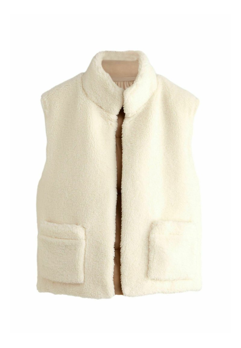 Gilet in pile color crema con colletto alto, chiusura frontale e due tasche a toppa. La texture è morbida e soffice, offrendo calore.