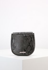 Malá tmavě šedá crossbody kabelka s texturou hadí kůže a kovovou destičkou se znakem Esprit na přední straně, vystavená na bílém podstavci.
