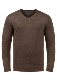 Brun v-hals sweater lavet af blødt strikmateriale. Har ribbede ærmekant og kant, med et lille mærket lædermærke nederst til venstre.