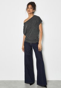 Czarny, błyszczący top typu off-the-shoulder o luźnym kroju i marszczonym pasie. Połączony z ciemnoniebieskimi dzwonami i butami na spiczastym czubku.