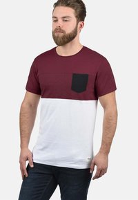 Bordeaux og hvid kortærmet T-shirt med en sort lomme, der har en struktureret øverste sektion og en glat nederste sektion.