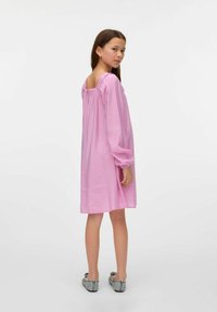 Vestido de algodón rosa con mangas largas, escote cuadrado y detalle fruncido en los hombros. La modelo lleva zapatos planos grises.