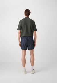 Mørkegrønn kortermet strikkegenser kombinert med marineblå treningsshorts. Modellen har på seg lyse sneakers og ankelstrømper.