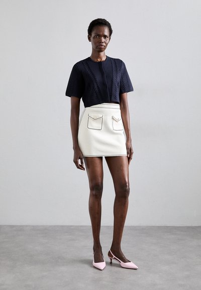 Top a maniche corte lavorato a maglia blu navy con gonna bianca dotata di due tasche frontali e cuciture nere, abbinato a tacchi a punta rosa.