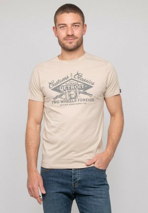 T-shirt en coton beige avec un graphique de moto, "Customs and Classics", et le texte "Detroit", associé à un jean en denim bleu.