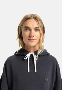 Donkergrijze hoodie met een trekkoord, voorzien van een voorzak en een klein logo. Zachte textuur en een ruime pasvorm. Katoenmengsel.