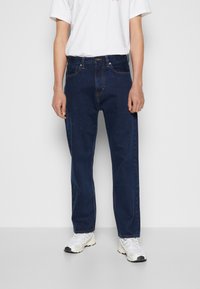 Mörka denimjeans med rak benmodell, som har en frontknäppning, fem fickor och subtila sömnadsdetaljer, bärs med vita sneakers.