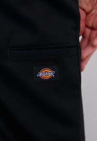 Sorte arbeidsbukser i stoff med et lite, brodert Dickies-logo på baklommen. Glatt tekstur med skreddersydd passform.