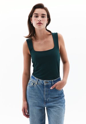 Débardeur à col carré vert foncé en tissu lisse, associé à un jean en denim clair taille haute avec un design classique à cinq poches.