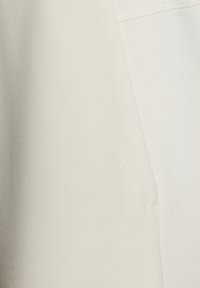 Off-white Kleidungsstück mit glatter Textur, ausgestattet mit eingeprägtem "CPNHGN" Branding an der Seite. Das Design ist minimalistisch und weist keine sichtbaren Muster auf.