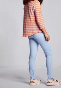 Gestreiftes langärmeliges Oberteil in Orange und Blau, kombiniert mit hellblauen Slim-Fit-Jeans und beigen Sandalen. Mit asymmetrischem Saum und lockerer Passform.