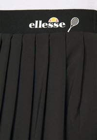 Černá skládací sukně s širokým elastickým pasem, na kterém je embosované logo "ellesse" a grafika tenisové rakety, vyrobená z lehkého materiálu.