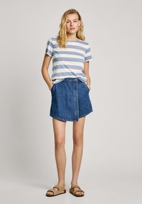 T-shirt en coton rayé bleu clair et blanc, associé à une jupe en jean bleue avec poches et fermeture à boutons devant.