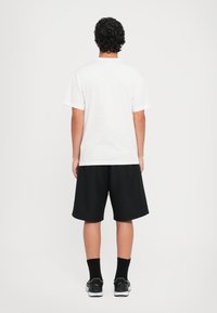 Hvit bomull T-skjorte med korte ermer, kombinert med svarte shorts. Merkbare detaljer inkluderer et enkelt design og en avslappet passform.