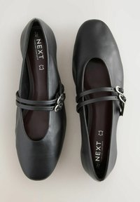 Musta nahkainen ballerina-malli, jossa on pyöristetyt varpaat, kaksi nauhaa jalkapöydän yli, hopea solki ja pehmustettu pohja.
