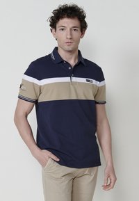 Tengerészkék és bézs csíkos pólóing, gallérral, rövid ujjal és logóval a mellrészen; texturált pamut keverékből készült.