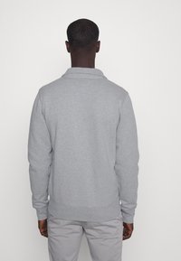 Sudadera gris con cuello, manga larga, puños y dobladillo acanalados, textura suave y detalles de diseño mínimos. Vista desde la parte posterior.