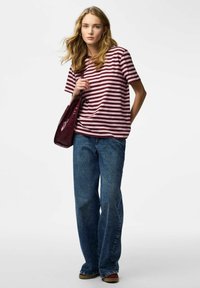 Striped short-sleeve shirt in burgundy and cream, paired with loose blue denim jeans and a glossy burgundy shoulder bag.